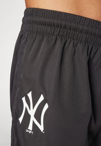 Pantalones cortos negros con cinturilla elástica, fabricados en una tela suave, que presentan un destacado logo blanco de los New York Yankees en la parte inferior izquierda.