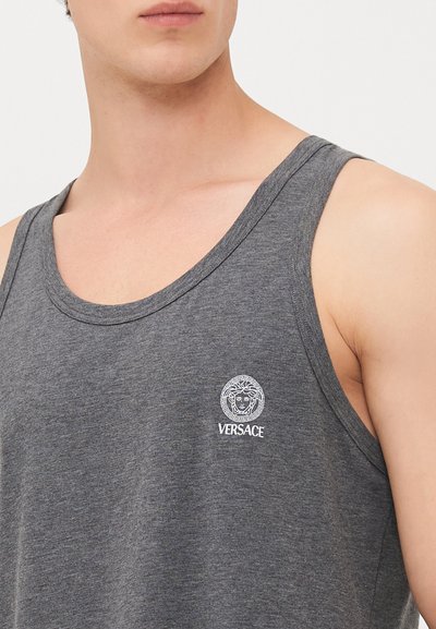 Pilkas medvilnės marškinėliai be rankovių su plačia kaklo iškirpte. Pagrindinėje dalyje yra baltas Versace logotipas ir Medūzos emblema.