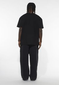 T-shirt nera oversize con vestibilità rilassata, maniche corte e scollo rotondo. Abbinata a pantaloni larghi scuri. Design minimalista.