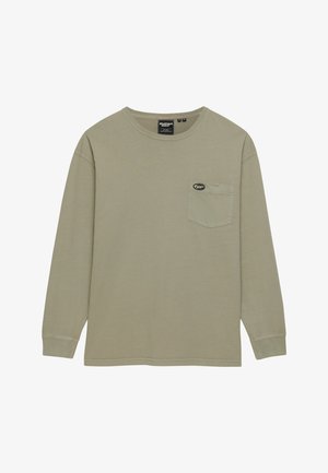 Beżowa koszulka z długim rękawem i okrągłym dekoltem, z kieszenią na piersi i małą owalną czarno-białą naszywką z logo.