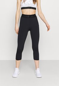 Leggings de sport noirs Capri avec une taille haute présentant une bande élastique texturée. Associés à un soutien-gorge de sport blanc, stylisés pour une tenue active.