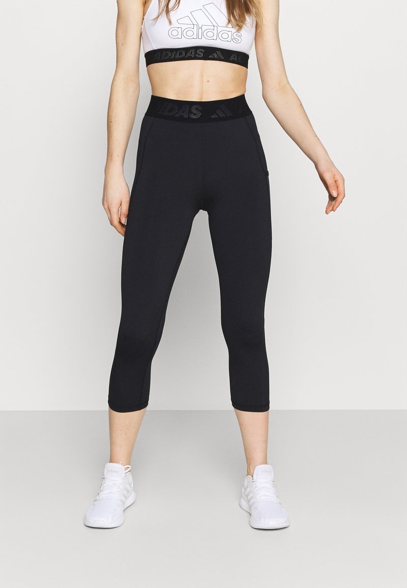 Leggings de sport noirs Capri avec une taille haute présentant une bande élastique texturée. Associés  à un soutien-gorge de sport blanc, stylisés pour une tenue active.
