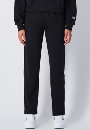 Pantaloni della tuta neri realizzati in tessuto morbido, con design a gamba dritta e vita elastica. Abbinati a scarpe da ginnastica bianche.