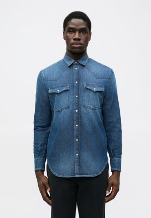 Camicia di jeans blu scuro con maniche lunghe, yoke appuntito, due tasche sul petto e chiusura con bottoni. Presenta una sottile texture a gradiente.
