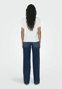 Haut blanc à manches courtes avec une coupe décontractée, associé à un jean large bleu foncé avec une texture subtile et des poches arrière.