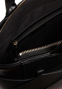 Εσωτερικό μαύρης δερμάτινης τσάντας με πολλές θήκες με φερμουάρ, εξαρτήματα σε χρυσή απόχρωση και υφή επιφάνειας.