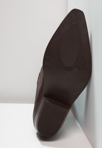 Zapato de cuero marrón con una suela de goma texturizada, que presenta una puntera ligeramente afilada y costuras detalladas a lo largo de los lados. Talla marcada como 41.