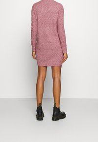 Abito lavorato a maglia a maniche lunghe in malva, design aderente, lunghezza a metà coscia. Abbinato a stivaletti neri con suola spessa e dettagli gialli.