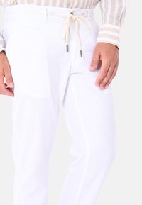 Pantaloni in lino bianco con vita a cordoncino in corda beige e punte in metallo. Tessuto leggero, vestibilità su misura e tasche laterali.