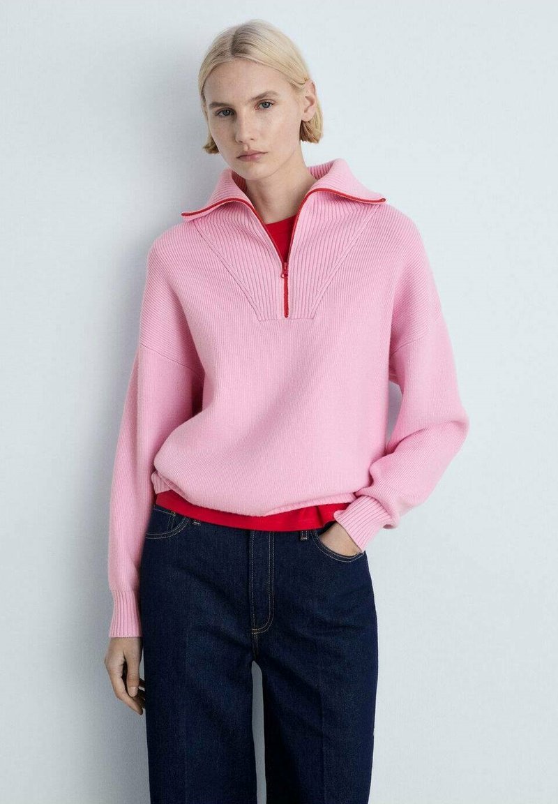 Rosa gerippter Pullover mit einem halbzipper Kragen, ausgestattet mit einer roten Innenschicht und weiten Ärmeln, kombiniert mit dunklen Jeans.