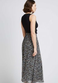 Un haut sans manches noir assorti à une jupe longue et fluide présentant un motif floral multicolore sur un fond sombre.