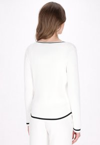 White ribbed sweater with long sleeves, featuring a black trim along the neck and cuffs. Smooth texture, fitted design, and simple style.