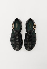 Zwarte vegan leren sandalen met gevlochten bovenwerk, open ontwerp en gouden gespaccent. Groene binnenvoering en gestructureerde zolen voor grip.
