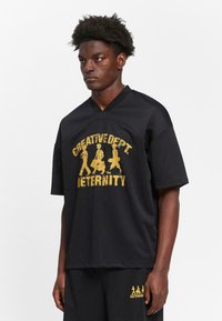Black mesh short-sleeve jersey featuring a gold graphic print that reads "CREATIVE DEPT. ETERNITY." V-neck design with relaxed fit.