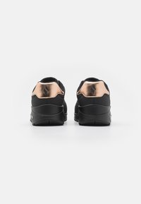 Black athletic shoes with a smooth, textured finish and a metallic rose gold accent on the heel. Curved sole design for flexibility.