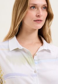 Camicia leggera con bottoni caratterizzata da un motivo ad acquerello in morbidi blu, verdi e gialli. Realizzata in tessuto liscio e leggero. Collo a punta.