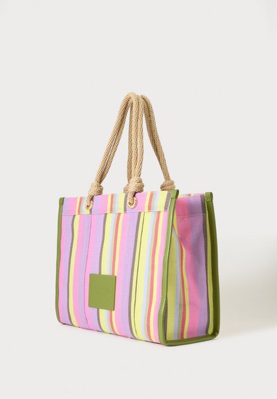 Sac cabas à rayures verticales multicolores, bordure verte, étiquette carrée verte et deux poignées épaisses en corde beige contre un fond uni.