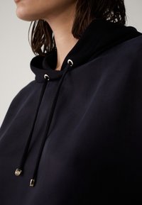 Navy hoodie met een gestructureerde stof, verstelbare trekkoorden met metalen accenten en een ontspannen pasvorm rond de halslijn.