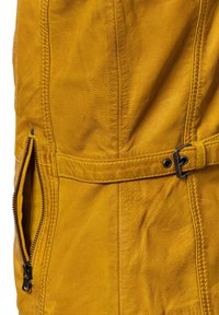 Gelber Lederjacke mit Reißverschlusstasche, genähten Nähten und einem taillierten Design mit einem glatten Textur.