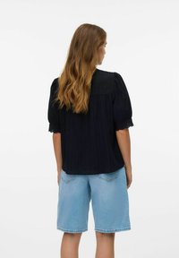 Svart texturerad blus med puffärmar, prydd med spetskant vid ärmsluten, tillsammans med ljusblå denimshorts.