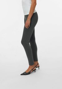 Leggings gris con canalé y un diseño ajustado, que presentan un dobladillo dividido y se combinan con zapatos de tacón destalonados negros y de punta.