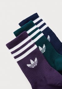 Calcetines de punto en púrpura, verde y azul marino, con rayas blancas y el logo de Adidas en los puños. Tejido texturizado con partes superiores acanaladas.