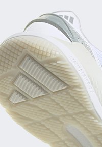 Białe buty sportowe z teksturowaną gumową podeszwą, z charakterystycznym wzorem trzech pasków Adidas i błyszczącym przezroczystym akcentem.