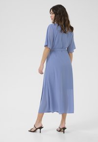 Vestido midi fluido de color azul claro, con mangas cortas, un cinturón atado en la cintura y una textura suave, combinado con sandalias negras de tacón.