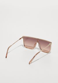 Overdimensionerte skjoldformede solbriller med gradient rosa linser og tynne gullmetallarmer, vist mot en hvit bakgrunn.