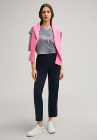 Roze sweatshirt over een gestreepte t-shirt met roze tekst, gecombineerd met navy broek en witte sneakers met beige accenten.