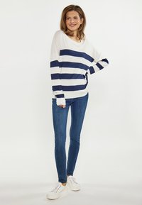 Top cu dungi alb-negru, cu mânecă lungă, croi lejer, asortat cu blugi skinny albaștri și adidași albi. Material neted, stil casual.