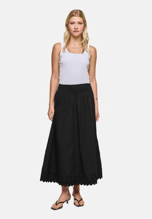 Woman with long blonde hair wears a white tank top, black ankle-length skirt with scalloped hem, and black sandals, standing facing forward.