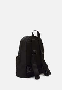 Černý batoh s texturovaným síťovaným panelem, polstrovanými ramenními popruhy a nastaviteln ými bočními přezkami. Zavírání na zip a minimalistický design.