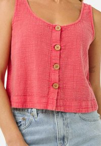 Top sin mangas color coral con un acabado texturizado, que presenta un cierre frontal con botones y cuatro botones de madera, además de un diseño corto.