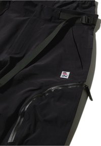 Pantaloni neri slim fit, realizzati in un tessuto texturizzato, con strap regolabile e una tasca laterale con zip. Patch del logo visibile sulla vita.