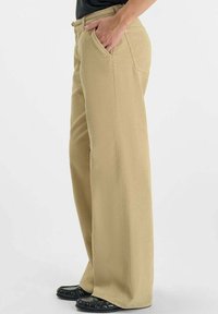 Beige corduroy wijde broek met een textuurfinish, voorzien van zijzakken en een hoge taille. Schoenen hebben een slank ontwerp en een gestructureerd oppervlak.