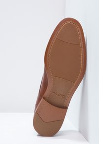 Chaussure habillée en cuir marron avec un dessus lisse, une semelle en caoutchouc et des accents texturés. Comprend le logo et des détails de couture sur la semelle.