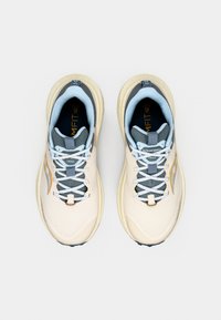 Beiget juoksukengät, joissa on verkkopäällinen, sinisiä yksityiskohtia ja harmaat nauhat. Kenkä on varustettu kuvioidulla pohjalla ja pehmeällä, pehmustetulla muotoilulla mukavuutta varten.