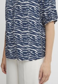 Top blu navy con motivo ondulato bianco, maniche corte a palloncino e vestibilità rilassata. Abbinato a pantaloni larghi di colore chiaro.
