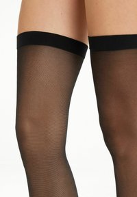 Bas noirs jusqu'à la cuisse avec une texture lisse et transparente et une large bande noire unie en haut. Pas de motifs visibles ni de matériel.