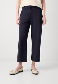 Marinebukser med rett ben-design, laget av et glatt stoff. Har sidelommer og kontrastsøm. Brukt med kremfargede loafers.