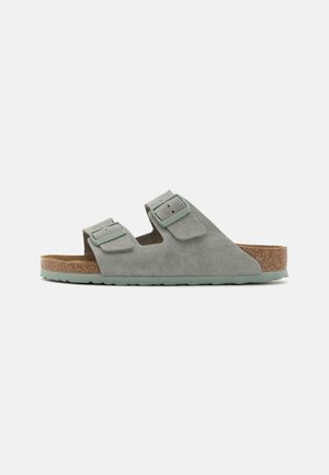 Sandales en suède gris avec deux sangles réglables, une semelle en liège et une semelle en caoutchouc vert texturé. Design simple, profil plat.