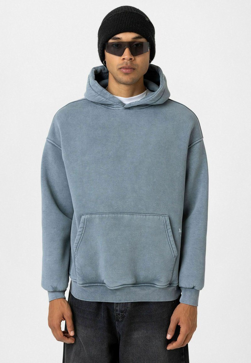 Blauwe hoodie van een katoenmix, met een voorzak, geribbelde boorden en een relaxte pasvorm. Draagt een zwarte beanie en een zonnebril.