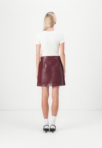 Burgunderfarget skinn mini skjørt med en glatt tekstur, med en bak glidelås og sømdetaljer. Kombinert med en hvit tettsittende t-skjorte.