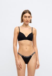 Čierna podprsenka s nastaviteľnými ramienkami a hlbokým výstrihom, v páre s čiernymi tangami s bielym pásom so značkou „KARL LAGERFELD“.