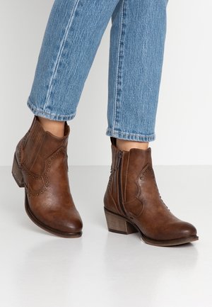 Ruskeat tekonahkaiset nilkkurit, joissa on terävä kärki, koristeompeleet, niittikoristelu ja pieni pino korko. Sivulla näkyvä vetoketjusuljin.