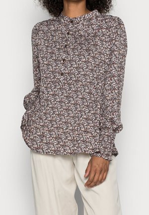 Woman wearing long-sleeve buttoned blouse with brown, white, and pink floral pattern paired with light beige pants.