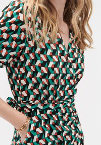 Geprinte jurk met geometrische patronen in groen, rood en wit op een zwarte achtergrond; taille gekraald met een strikdetail.