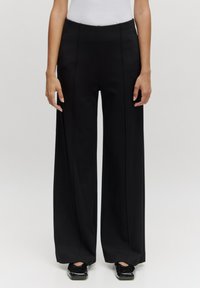 Zwarte wijde broek van soepel stof, met een hoge taille, rechte naden en een sleeplengte ontwerp. Klassieke silhouet met minimale details.