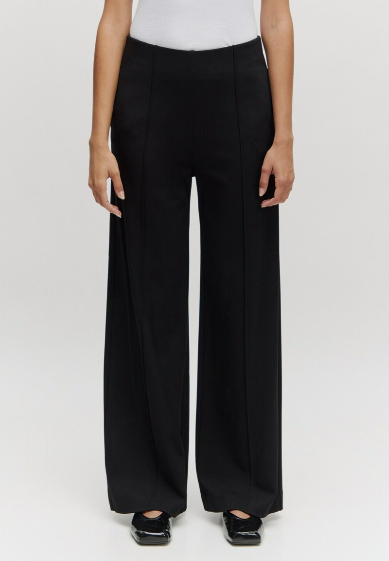Zwarte wijde broek van soepel stof, met een hoge taille, rechte naden en een sleeplengte ontwerp. Klassieke silhouet met minimale details.